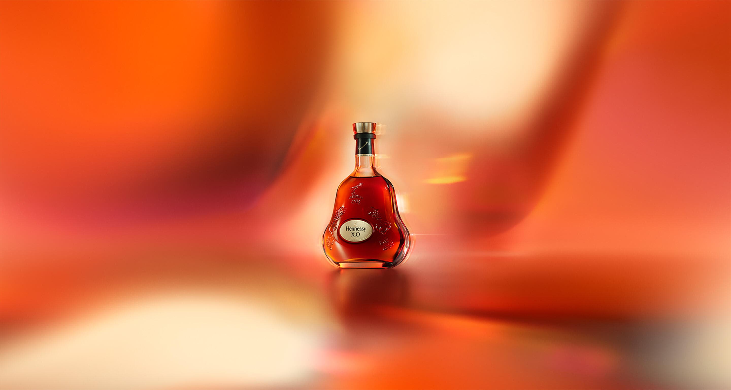 Bouteille de cognac Hennessy X.O sur un fond rouge orangé