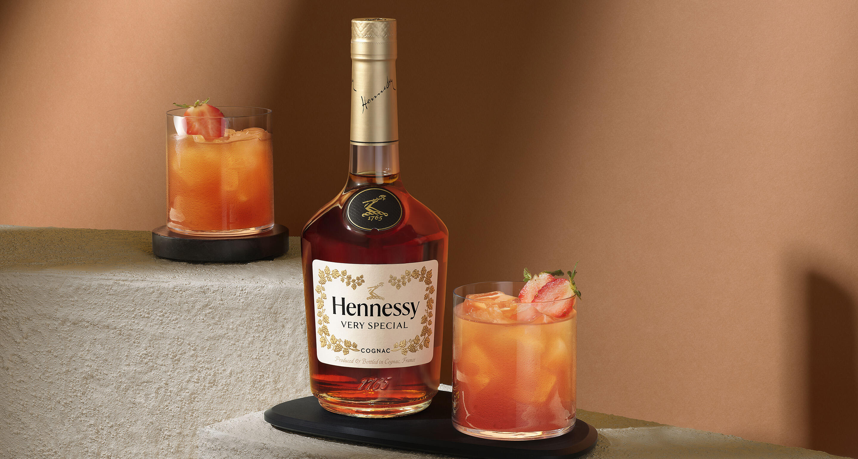Bouteille de cognac Hennessy V.S à côté d'un verre de cocktail à la fraise et à la goyave