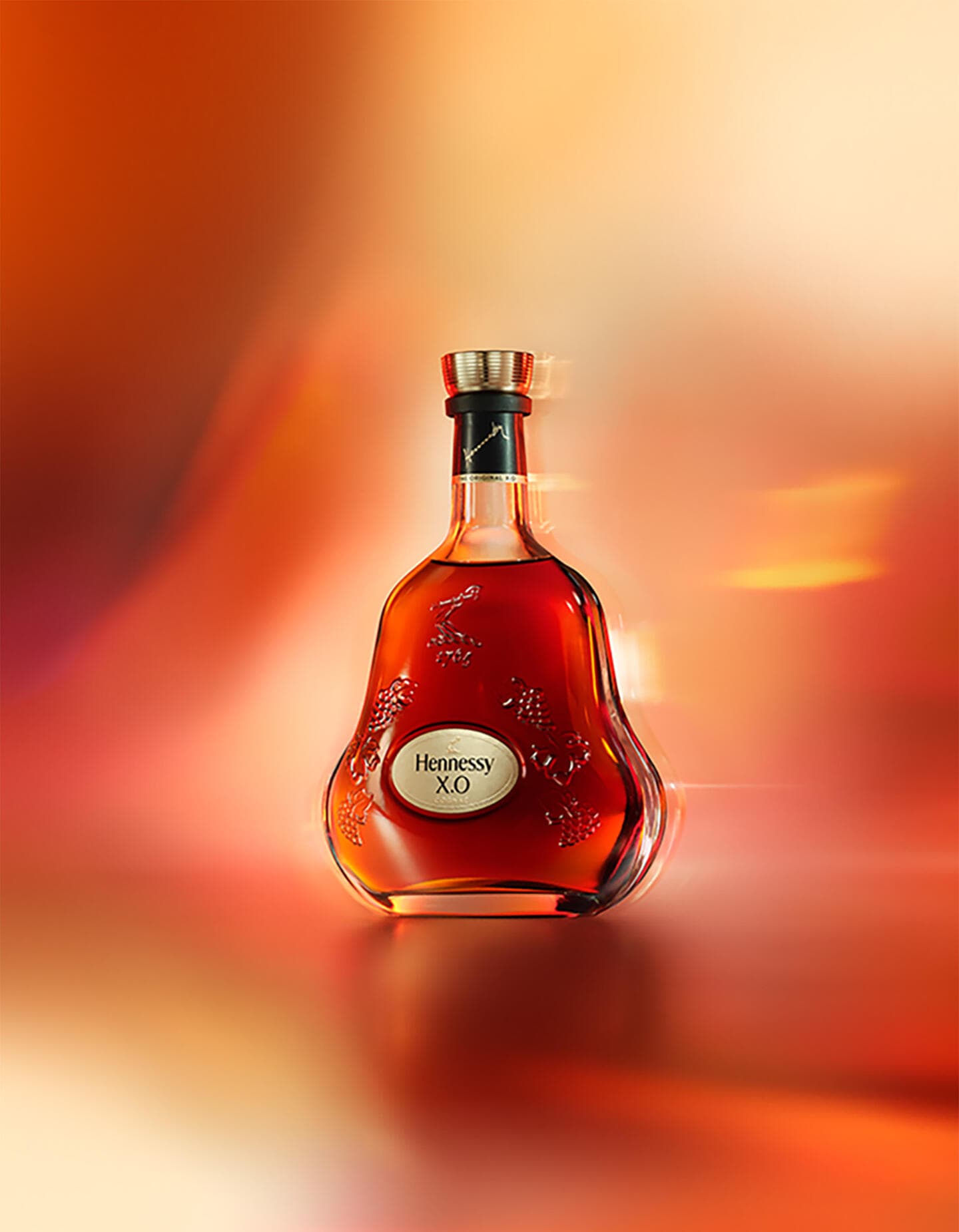 Bouteille de cognac Hennessy X.O sur un fond rouge orangé