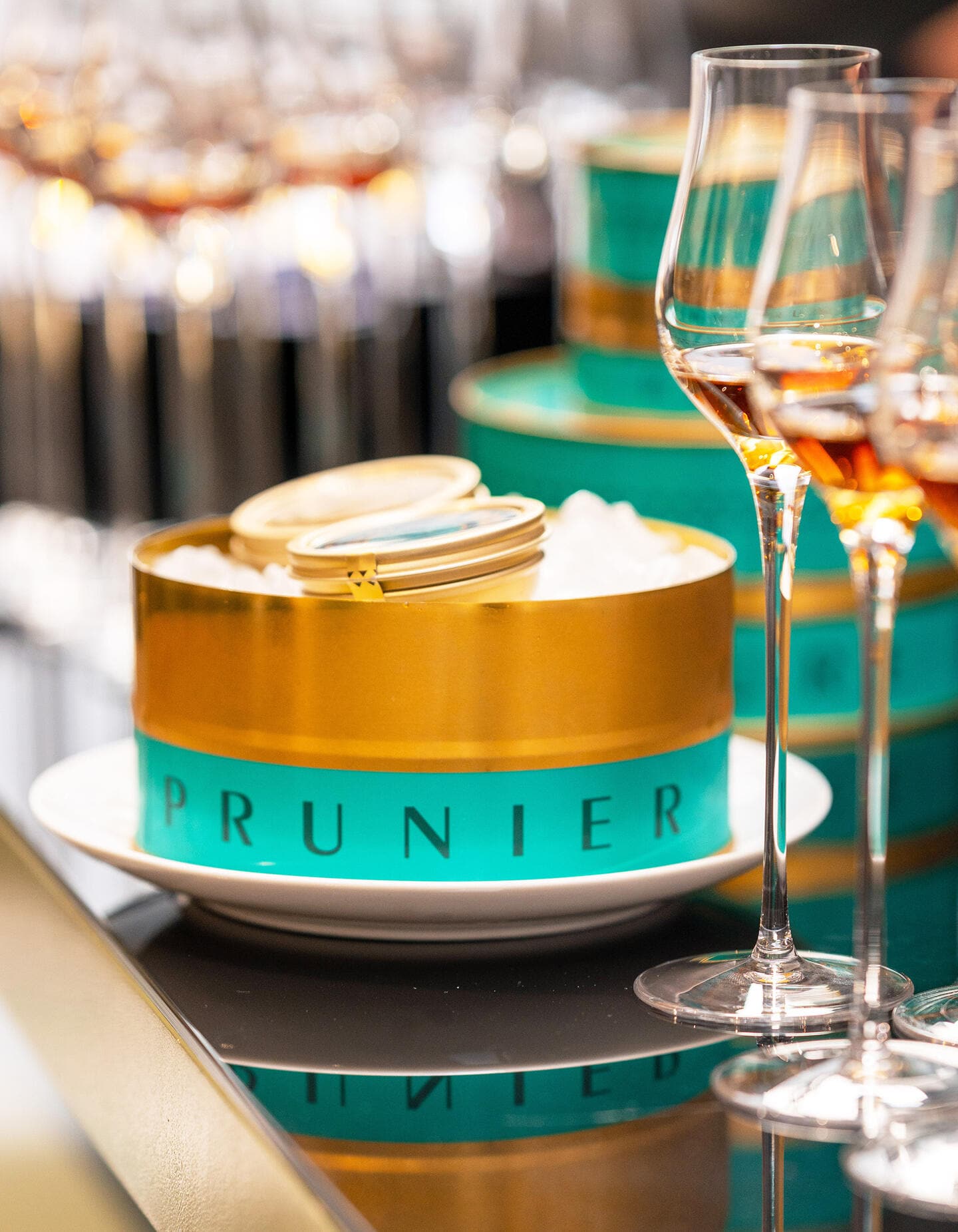 Boite de caviar Prunier turquoise et doré, à côté de verres de cognac Hennessy