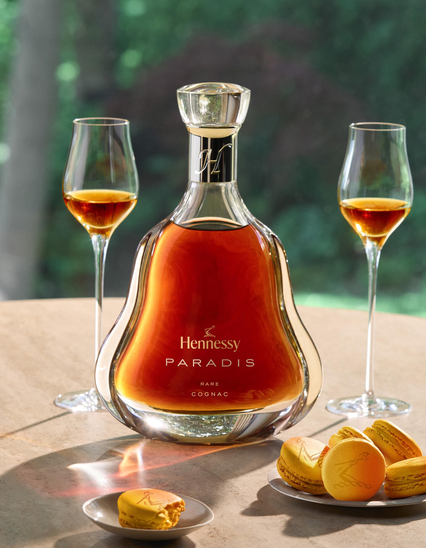 Carafe de Hennessy Paradis upgrade posée sur une table, à côté de 2 verres de cognac et d'une assiette de macarons au fruit de la passion