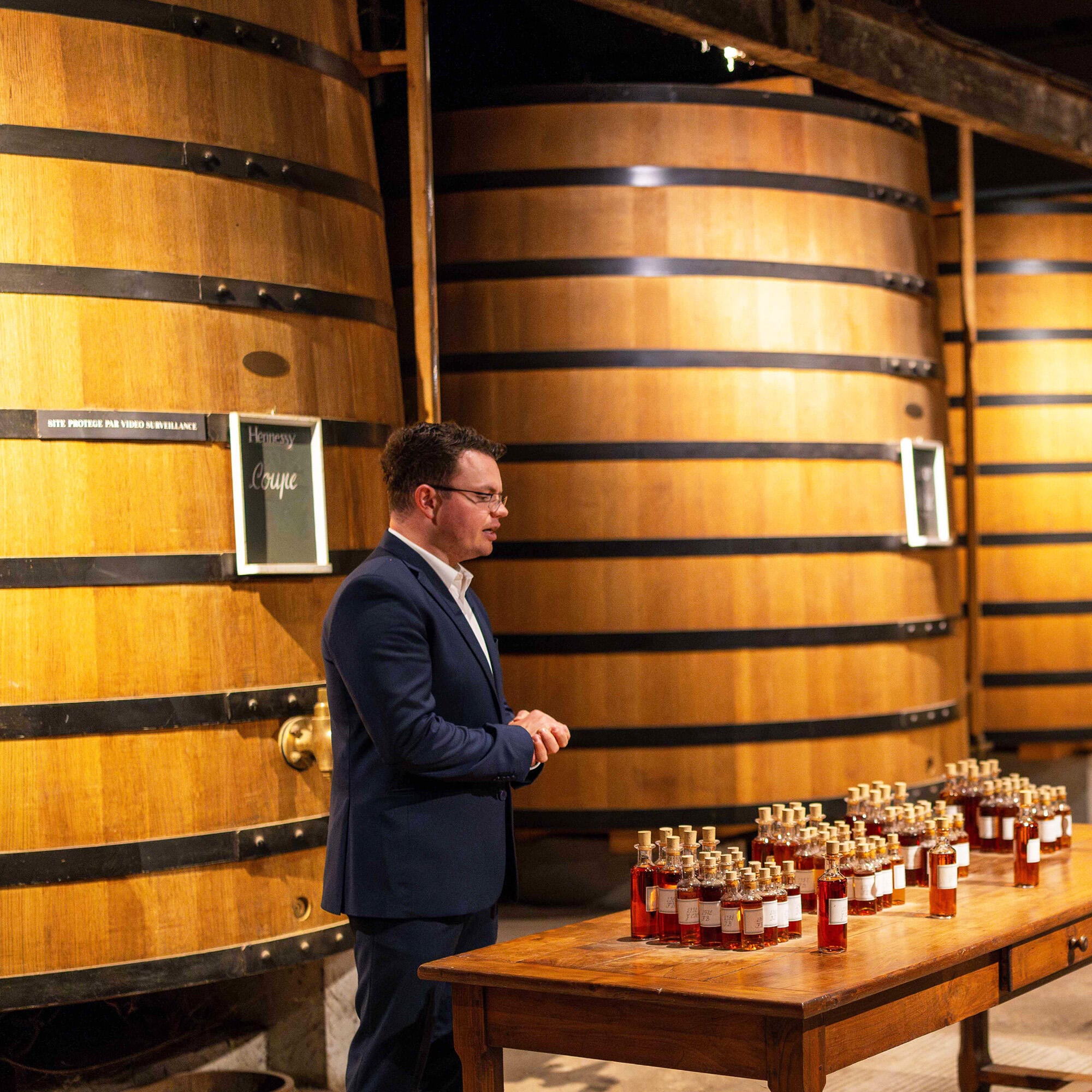 Guide Hennessy dans l'un de nos chais de maturation, debout devant des foudres en chêne, expliquant l'art de l'assemblage devant des dizaines de petits flacons de verre contenant chacun des eaux-de-vie différentes