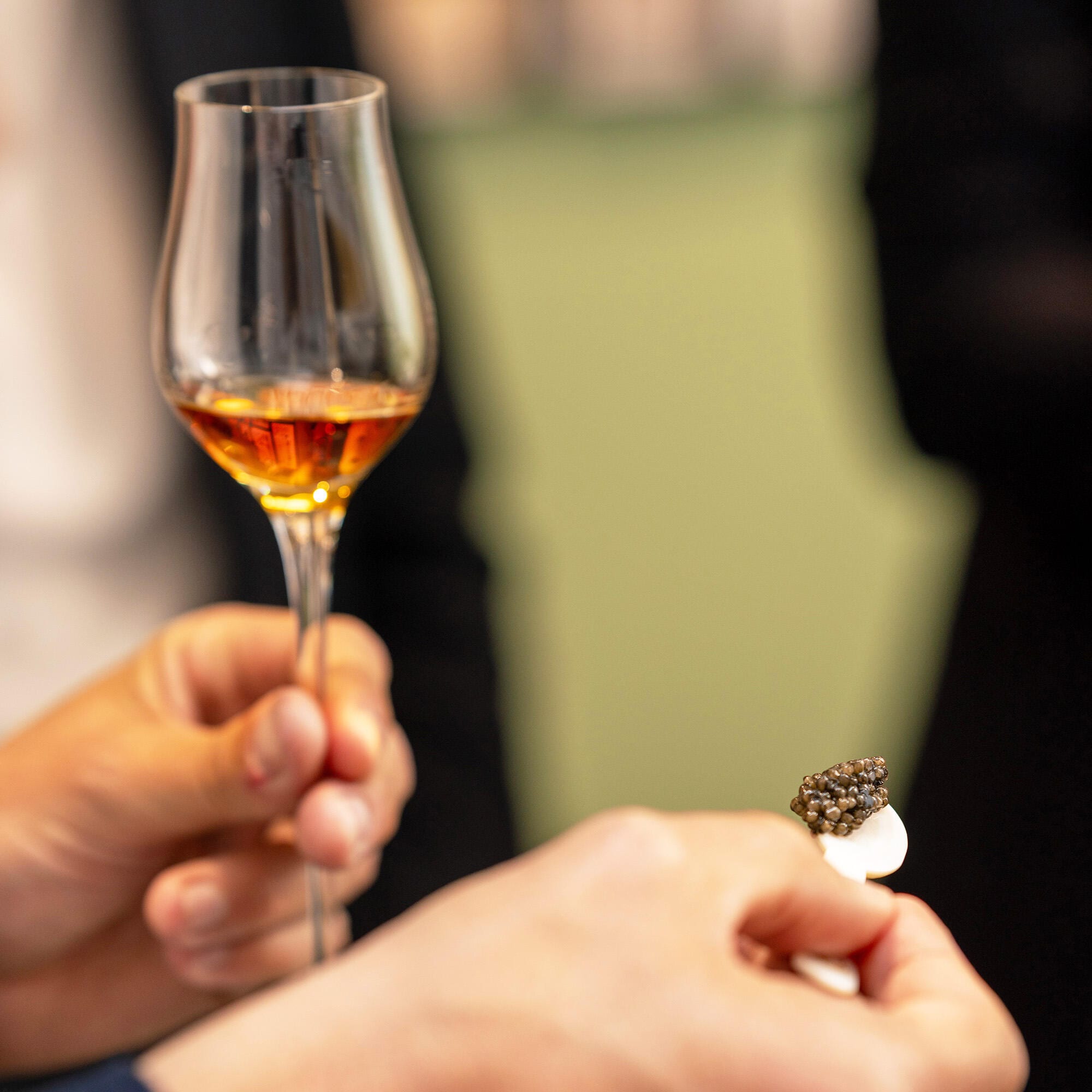 Un client tiens dans sa main gauche un verre de cognac Hennessy, et dans la droite, une cuillère de nacre blanche avec des grains de caviar