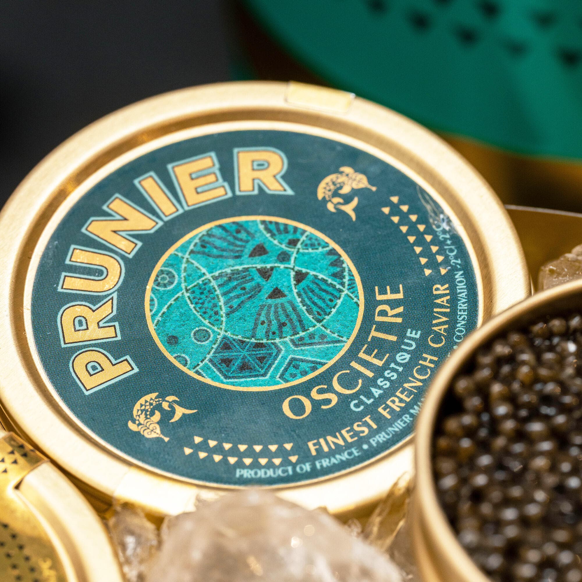 Boite de caviar Prunier Osciètre Classique, turquoise et dorée, sur de la glace pilée