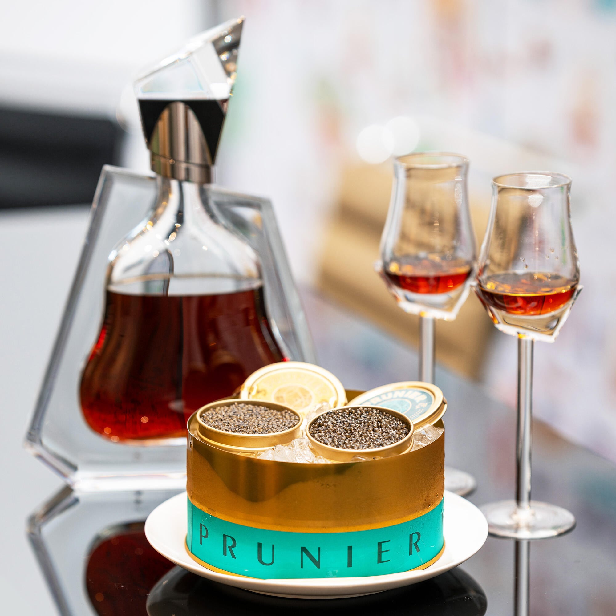 Carafe de cognac Richard Hennessy à côté d'une boite de caviar Prunier turquoise et dorée, avec 2 verres de cognac