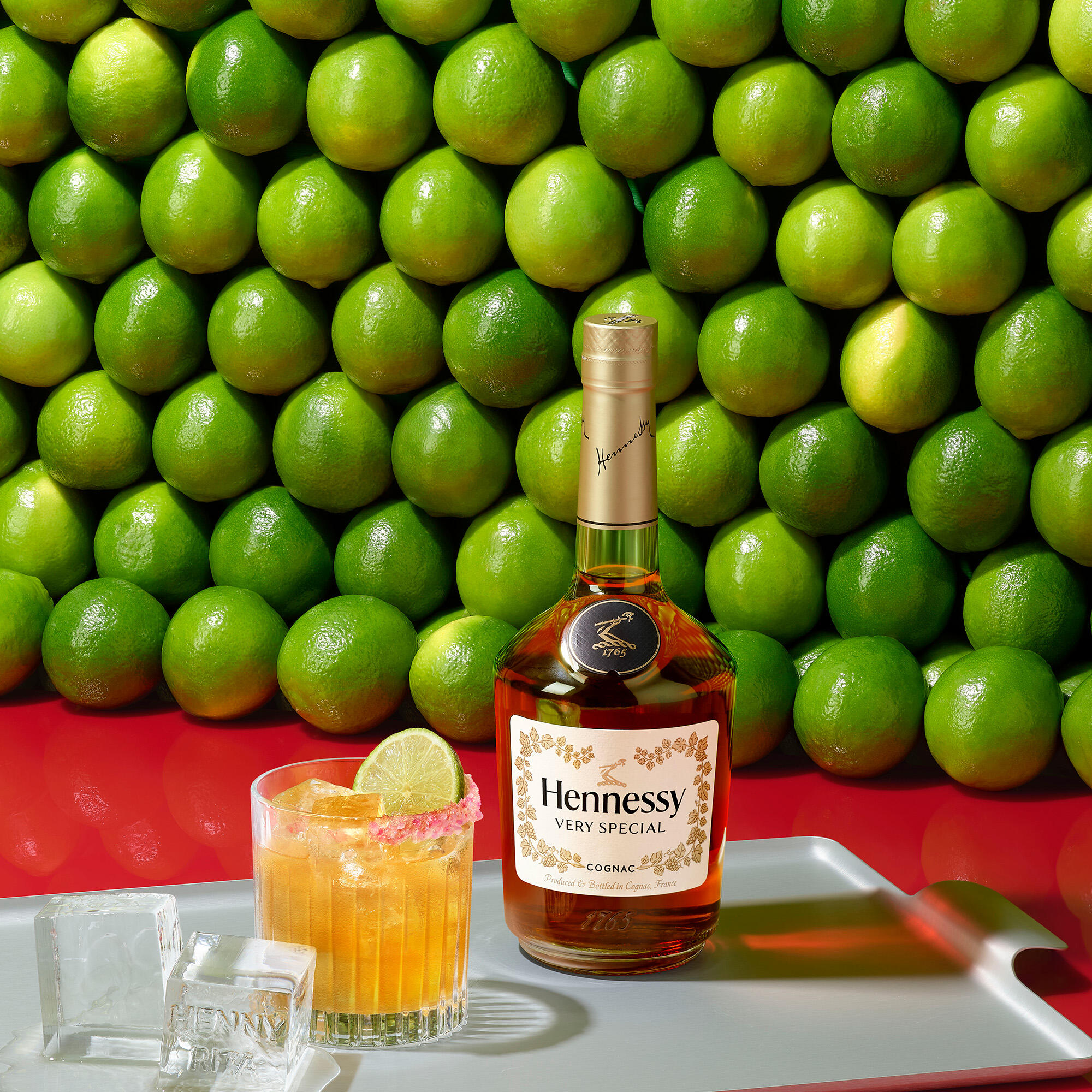 Cocktail Hennessy margarita à côté d'une bouteille de Hennessy V.S, devant un mur de citrons verts