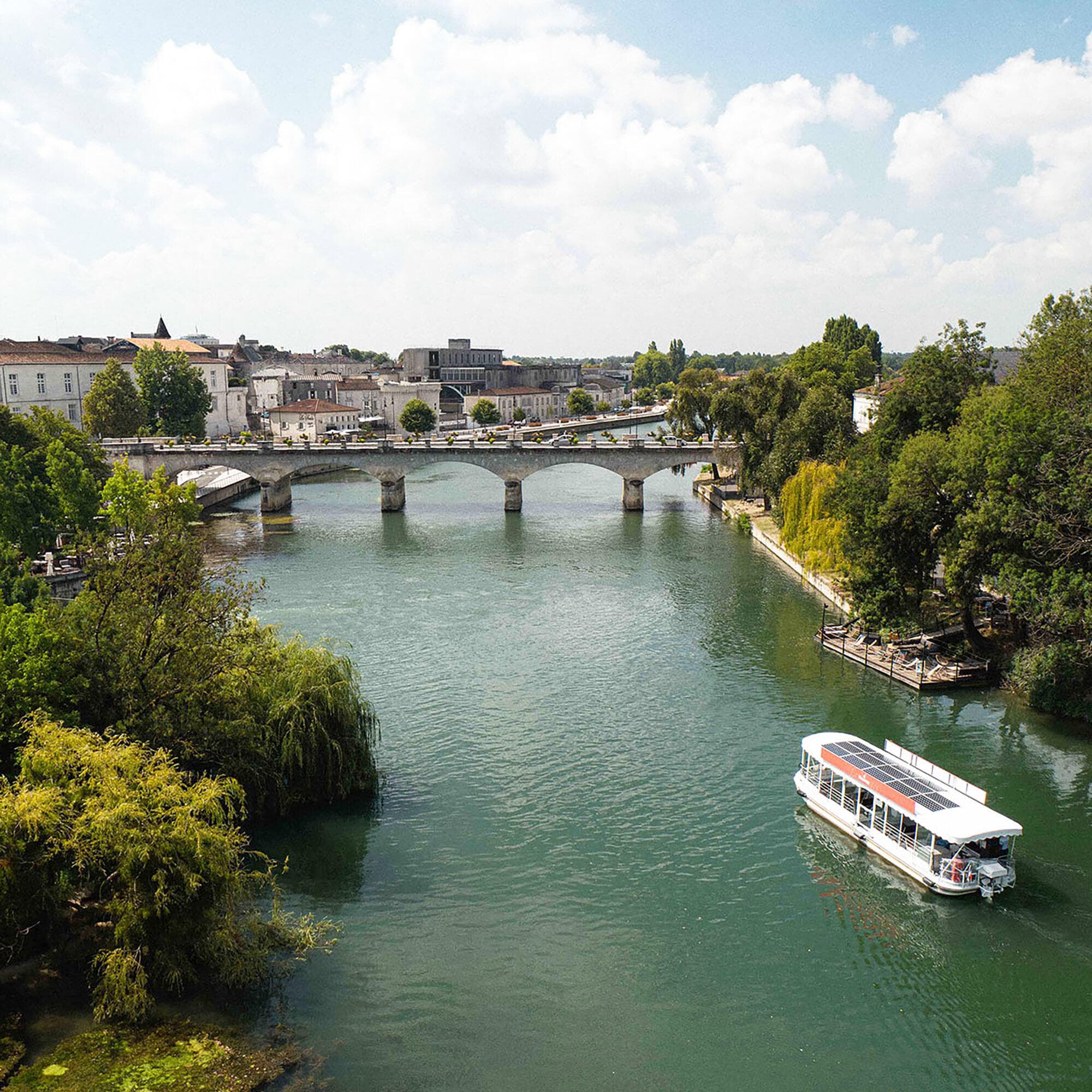 Vue aérienne de la Charente avec un bateau Hennessy navigant dessus, avec en toile de fond le Pont Neuf de Cognac, les Quais Hennessy et le centre historique de la ville