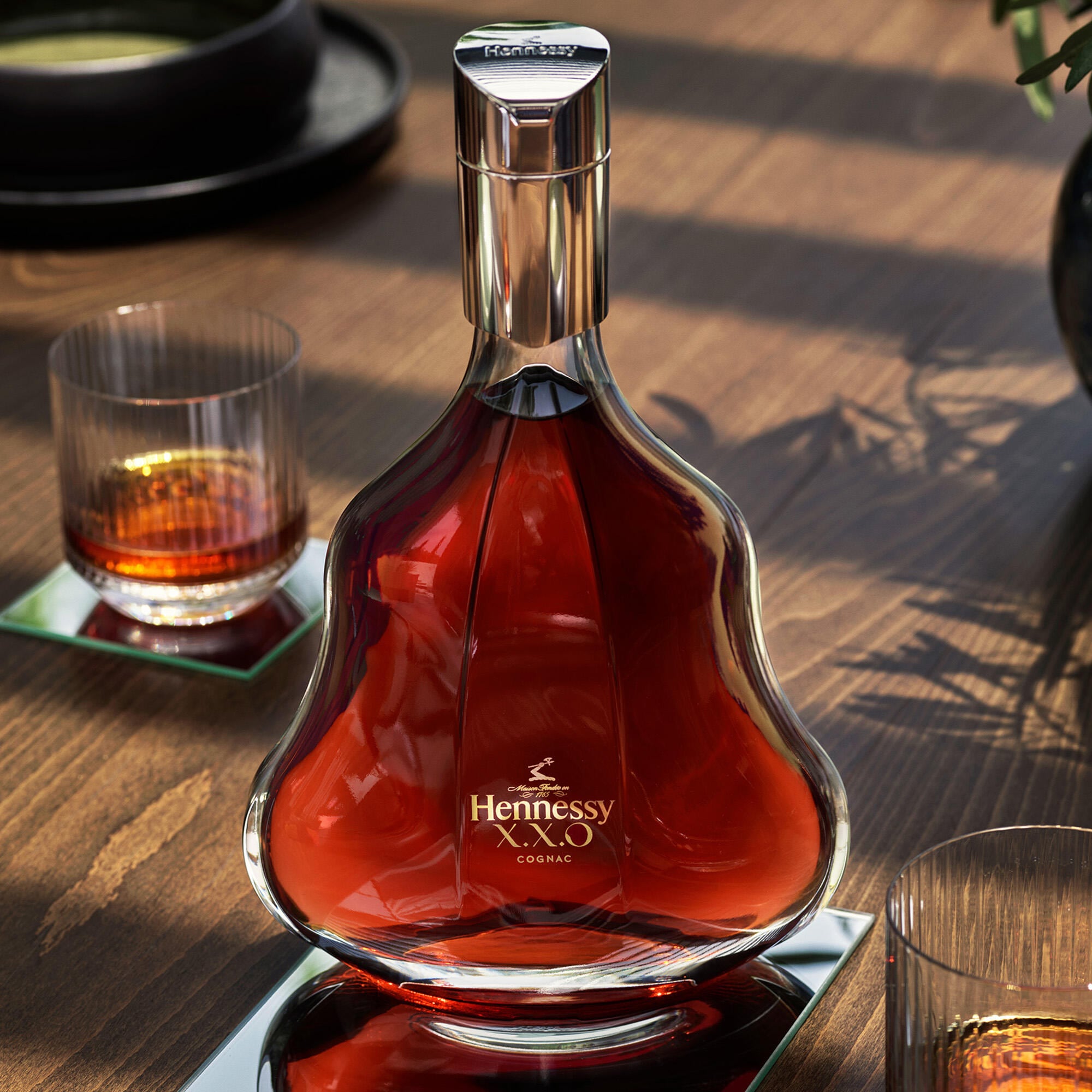 Carafe de Hennessy X.X.O posée sur une table en bois, à côté d'un verre de cognac