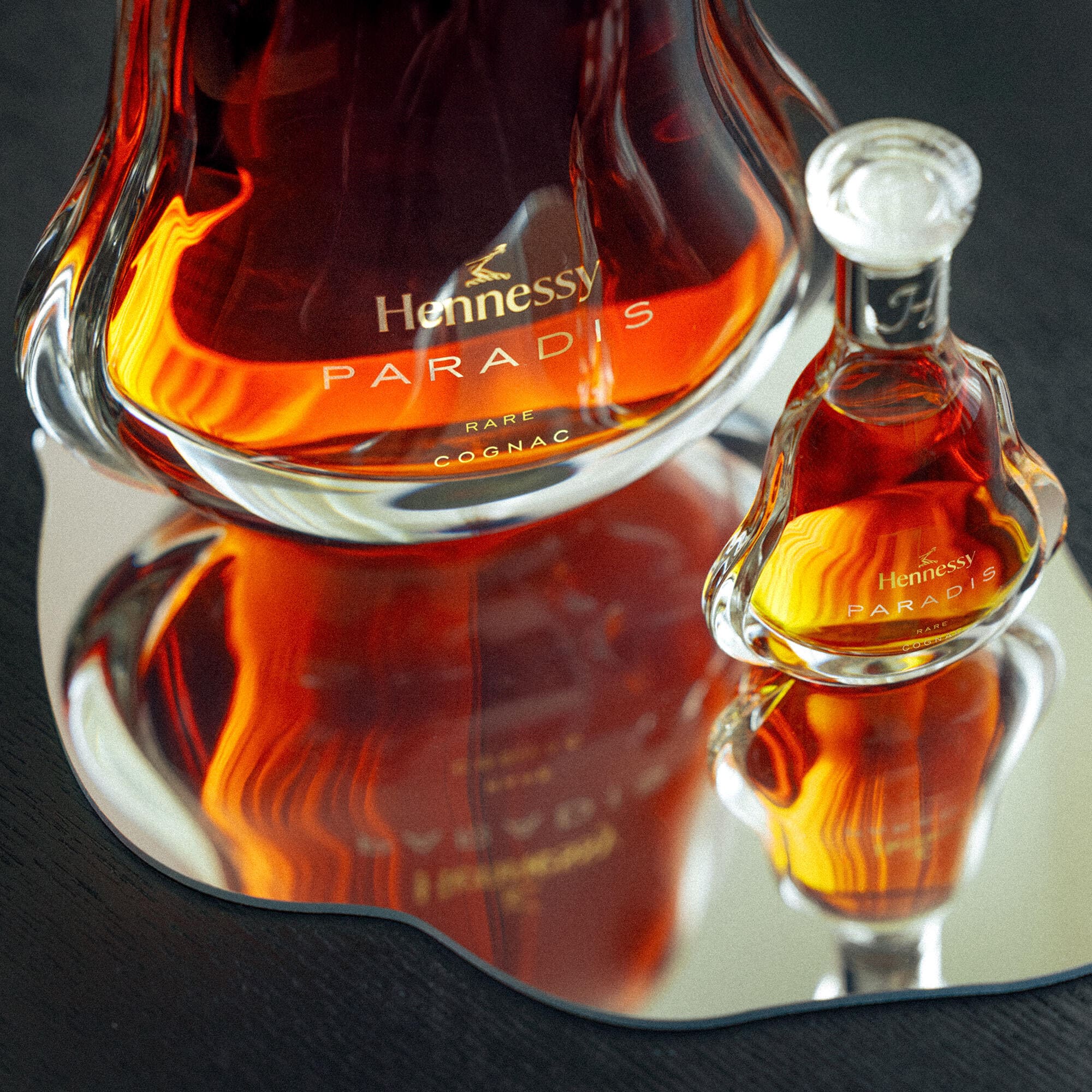 Carafe de cognac Hennessy Paradis (upgrade), posée sur un plateau effet miroir, à côté d'une carafe de Hennessy Paradis Mini (5cl)