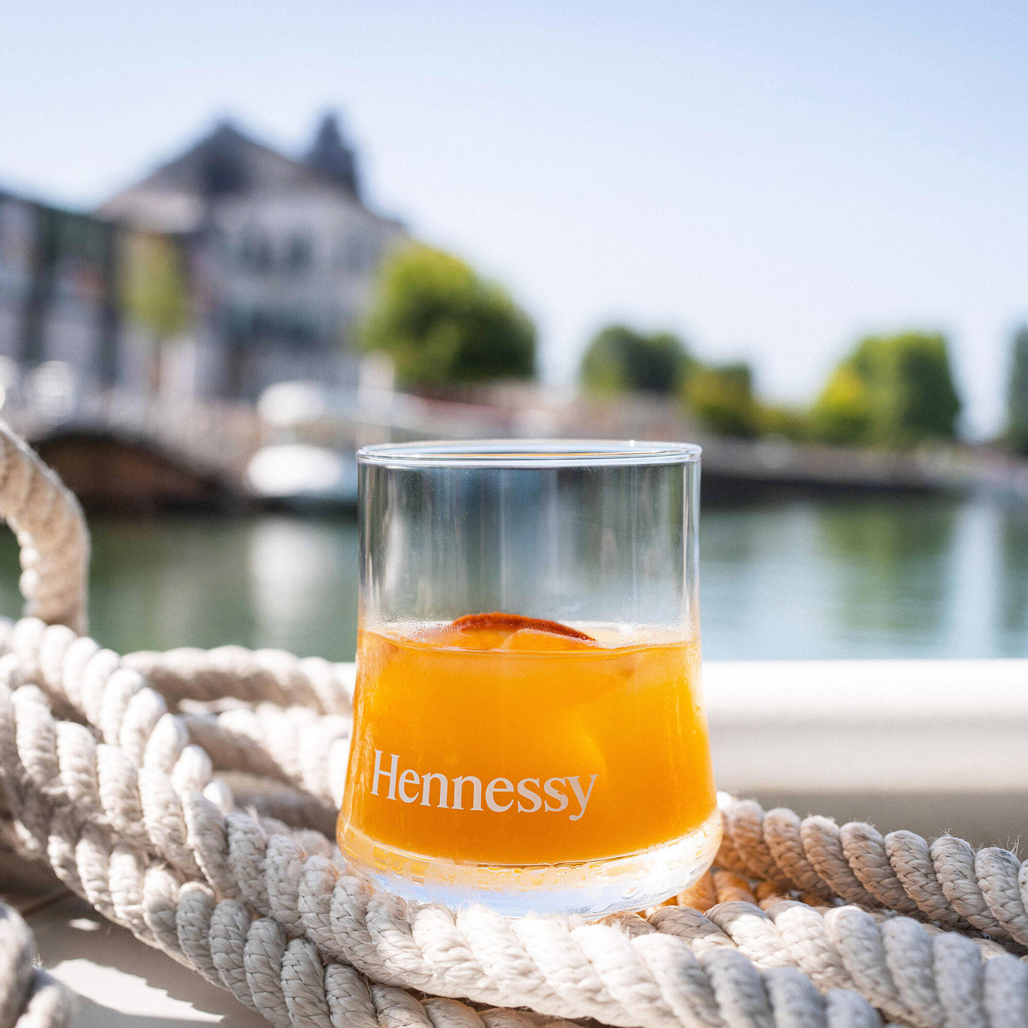 Un verre de cocktail au cognac Hennessy est posé sur un bateau, lors d'une traversée de la Charente, avec le bâtiment des Visites Hennessy en arrière-plan